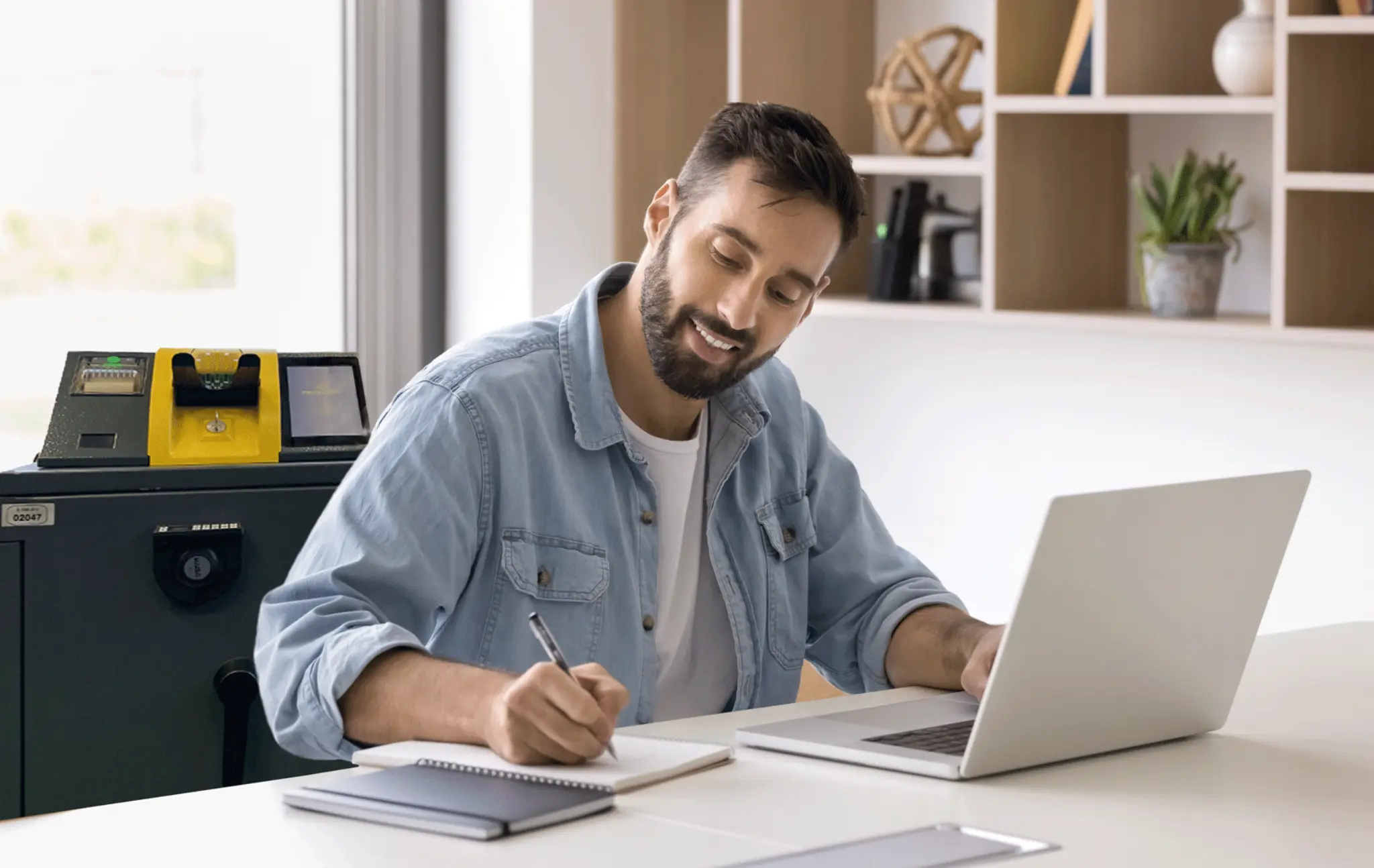 Mann sitzt im Büro am Laptop, im Hintergrund ein Smart Safe